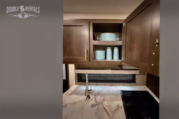 Well-equipped RV rental kitchen featuring open wooden cabinets with blue dishes, a modern sink, and stovetop.. KZ Sportster 2021