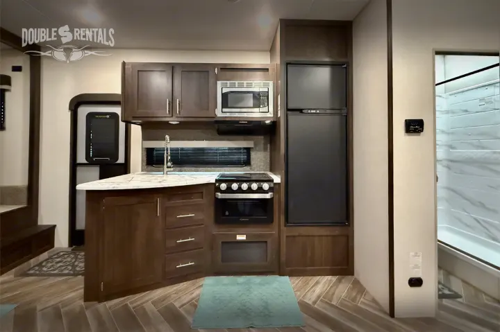 This RV rental features a modern kitchen with dark cabinets, a microwave, stove, refrigerator, and an island with a sink.. KZ Sportster 2021