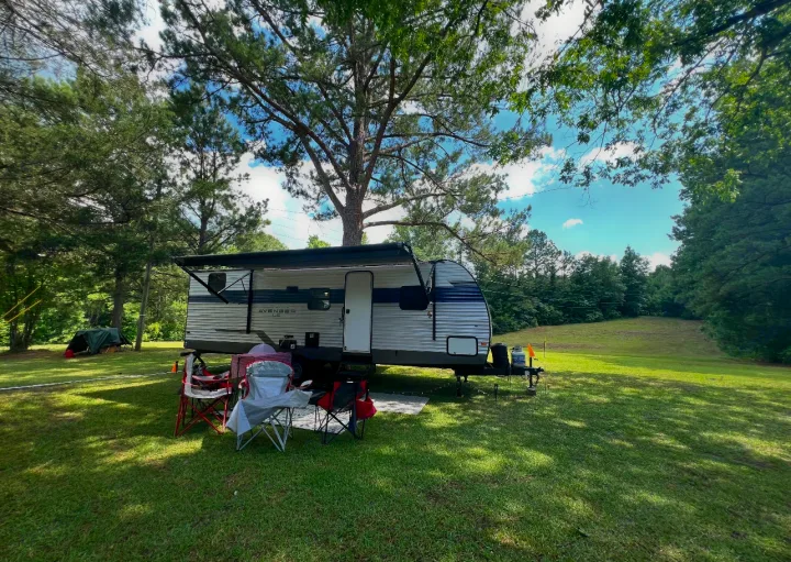 An RV rental, an Avenger travel trailer, is parked under a tree with an awning, chairs, and table for camping.. Avenger LE 2022