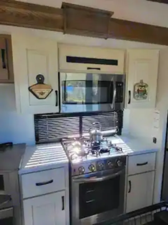 Bright RV rental kitchen bathed in sunlight, featuring a microwave, gas stove, and white cabinets for mobile living.. Alliance RV Paradigm 2024