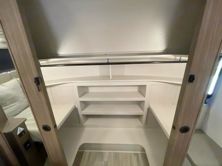 Compact sleeping and storage area in an RV rental, with built-in white shelves and a top black hanging rod.. Alliance RV Paradigm 2024