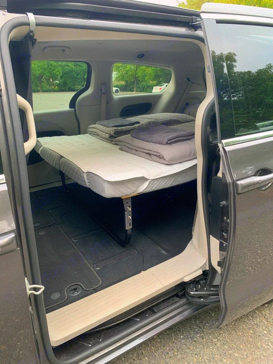 Inside an RV rental alternative: a minivan transformed into a cozy sleeping space with an elevated bed and bedding.. Chrysler Voyager 2022