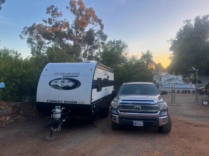 A shiny white Cherokee Wolf Pup RV rental is parked next to a grey Toyota Tundra truck on a dirt lot, ready for adventure.. Forest River Wolf Pup 2025
