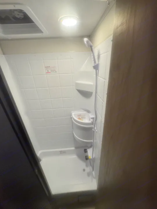 Compact white shower in an RV rental, featuring a handheld showerhead and small corner sink. Ideal for travel.. Forest River Wolf Pup 2025