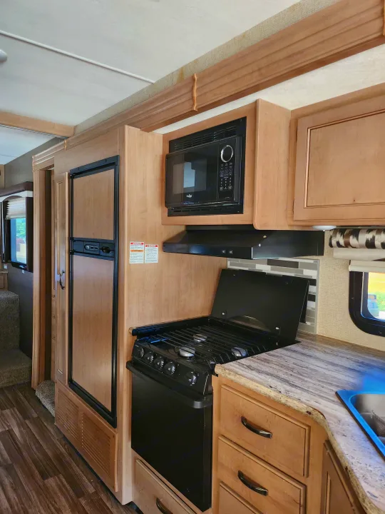 RV rental kitchen: light wood cabinetry, modern microwave, stove, refrigerator, and granite-look counters.. Thor A.C.E. 2018