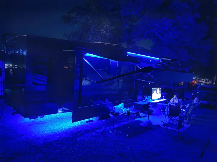 Enjoying a vibrant night at the campsite with an RV rental, featuring cool blue lights, outdoor seating, and a screen for entertainment.. Keystone RV Cougar 2024
