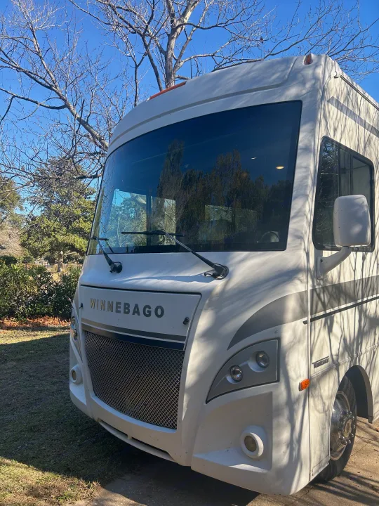 Front view of a white Winnebago RV, reflecting trees in its windshield. Perfect for an RV rental getaway.. Winnebago Intent 2018
