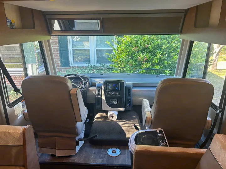 RV rental interior shows front cockpit: driver/passenger seats, dashboard, and exterior house view through the windshield.. Winnebago Intent 2018