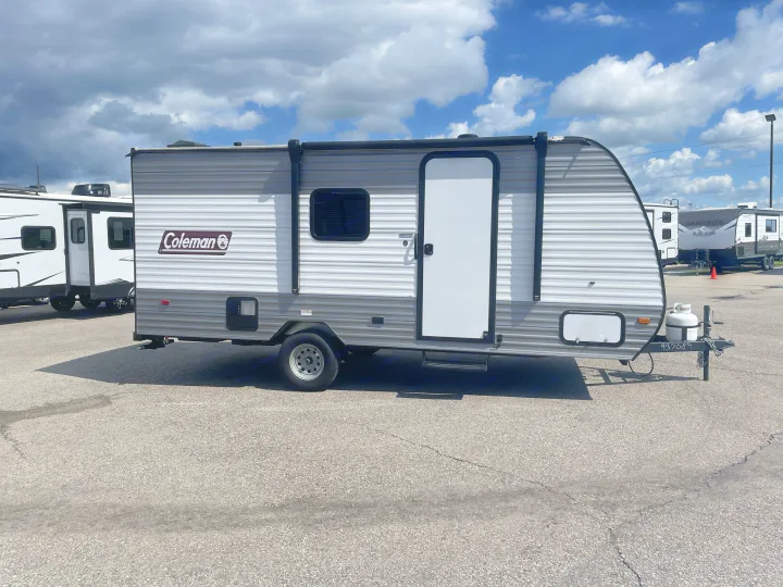 A sleek gray & white Coleman travel trailer, ideal for an rv rental, is parked on asphalt under a cloudy sky.. Dutchmen Coleman Lantern LT 17B 2024