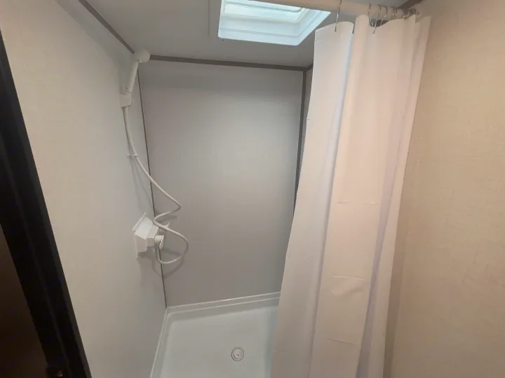 Inside an RV rental shower, featuring a handheld showerhead, white curtain, and overhead skylight.. Dutchmen Coleman Lantern LT 17B 2024