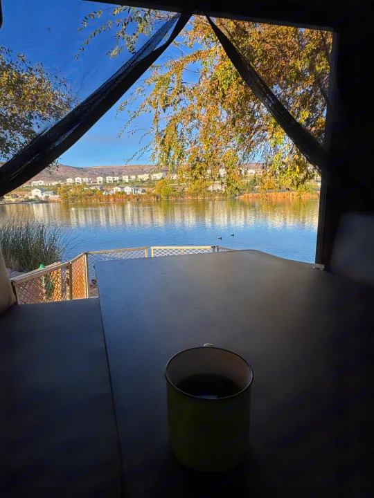Inside an RV rental: a warm cup of coffee overlooks a calm lake, distant houses, and autumn trees.. Forest River Cherokee Grey Wolf 2016