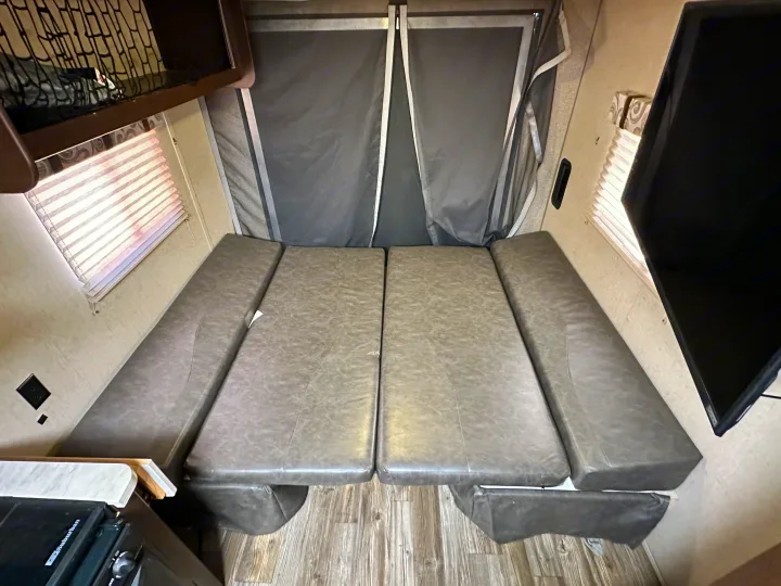 Cozy RV rental interior with grey convertible bench seating, stove, TV, and pop-out rear tent walls.. Forest River Cherokee Grey Wolf 2016