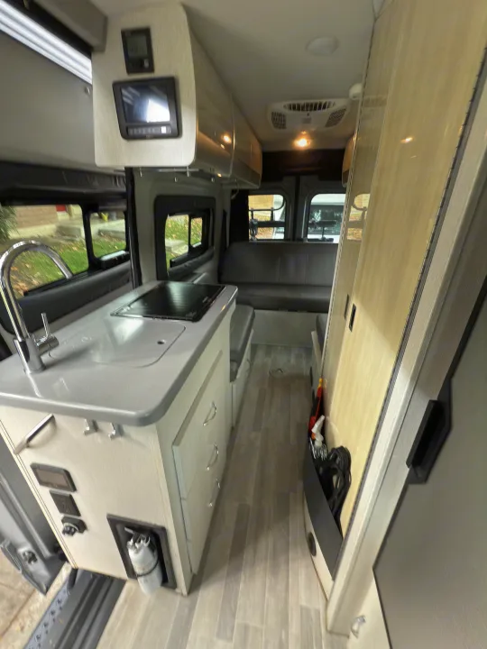 View inside a modern RV rental, featuring a compact kitchen, dinette, and overhead storage in this well-equipped camper.. Thor Tranquility 2023