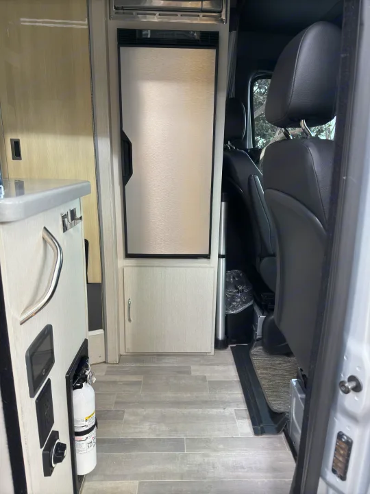 RV rental interior: kitchenette, refrigerator, fire extinguisher, and front passenger seats. Compact, functional design.. Thor Tranquility 2023