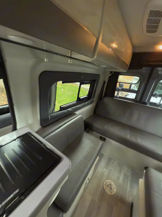 Spacious RV rental interior featuring modern gray seating, a compact kitchen area, and large windows. Perfect for trips!. Thor Tranquility 2023