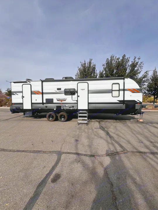 A white Wildwood travel trailer with black accents, ideal for an RV rental adventure, parked on an asphalt lot.. Forest River Wildwood 2022