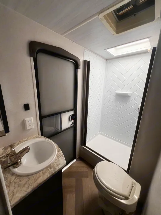RV rental bathroom features a sink, toilet, and modern shower with herringbone pattern walls. A compact & functional space.. Forest River Wildwood 2022