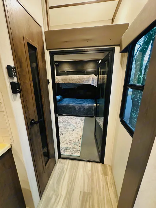 Inside this RV rental: A bright hallway with light wood floors opens to a cozy bunk bed room featuring two beds.. Alliance Valor 40v13 2022