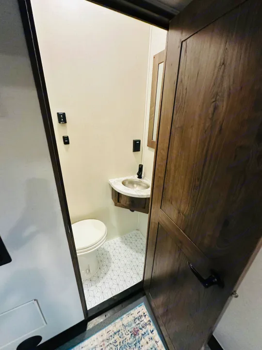 RV rental bathroom: A compact space with a toilet, corner sink, and modern geometric floor tiles, seen through an open wood-grain door.. Alliance Valor 40v13 2022