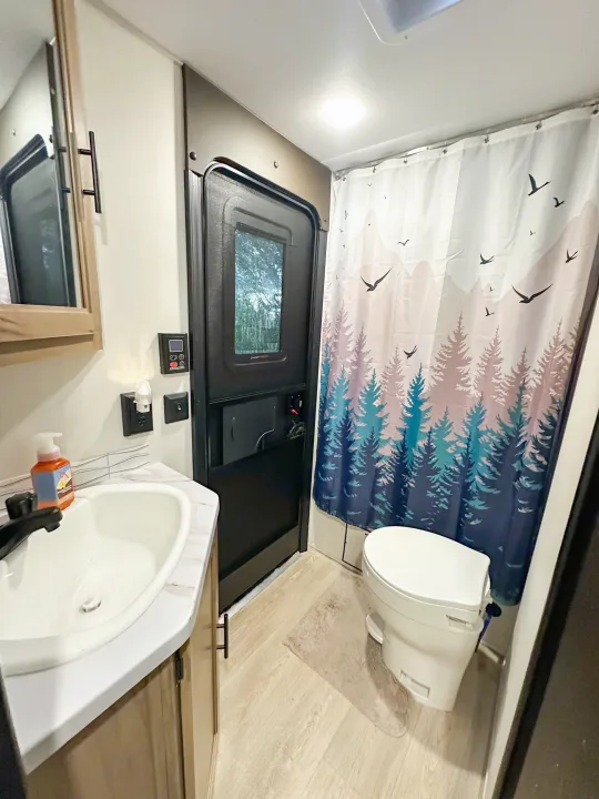 Discover a functional RV rental bathroom: equipped with a sink, toilet, and a vibrant forest-themed shower curtain.. Forest River Grey Wolf 26 DBH 2025