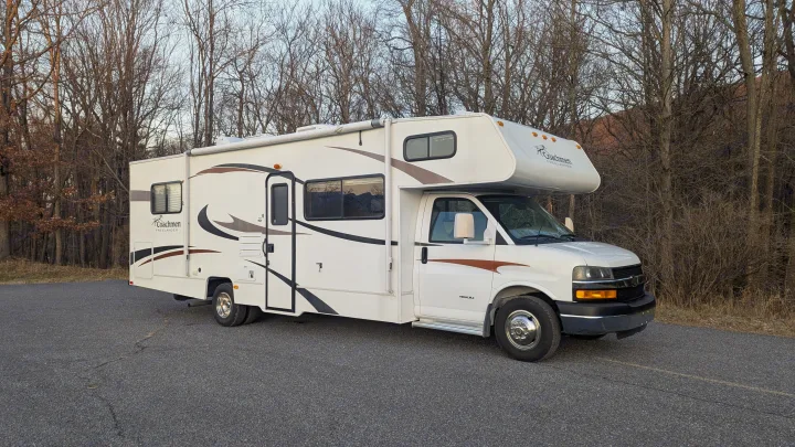 Coachmen Freelander Class C RV rental parked on asphalt with a forest of bare trees in the background.. Forest River Coachmen Freelander 2013