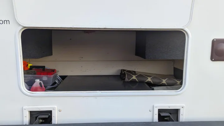 Inside an RV rental's accessible storage compartment, showing tools, a red liquid jug, and a rolled mat for travel.. Forest River Coachmen Freelander 2013