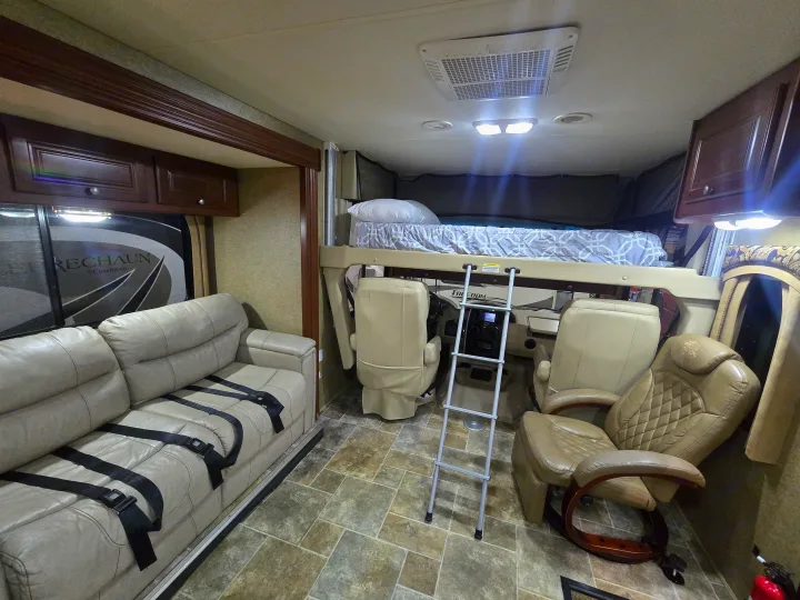 Interior of an RV rental showing a comfortable living area with sofa & seatbelts, front cockpit, and accessible overhead bunk bed.. Thor Motor Coach Miramar 2014