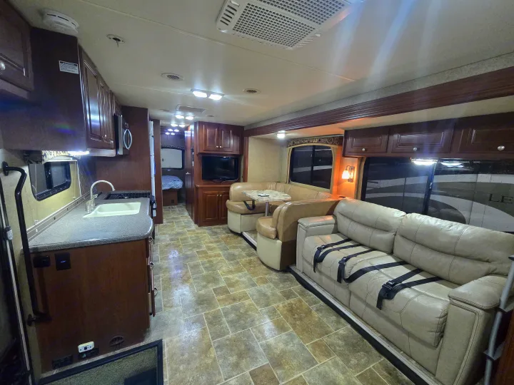 Explore this spacious, modern RV rental interior featuring a full kitchen, comfortable living area, and a glimpse of the bedroom.. Thor Motor Coach Miramar 2014