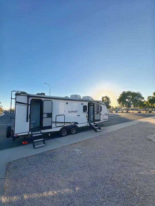 White 'Sunset Trail' RV rental parked with steps down, doors open, bathed in golden hour light. Ready for camping adventures.. Keystone RV Sunset Trail 2024
