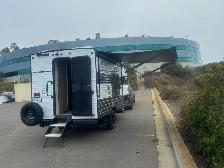 This white and black Wolf Pup travel trailer, an ideal RV rental for camping, has its door open and awning out in a parking lot.. Forest River Wolf Pup 2025