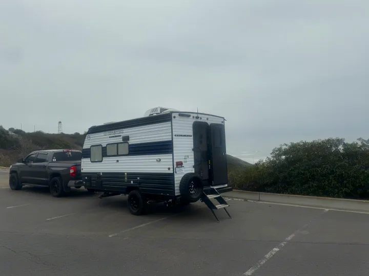 White & black Cherokee Wolf Pup RV rental and pickup truck parked by the ocean on a cloudy day.. Forest River Wolf Pup 2025
