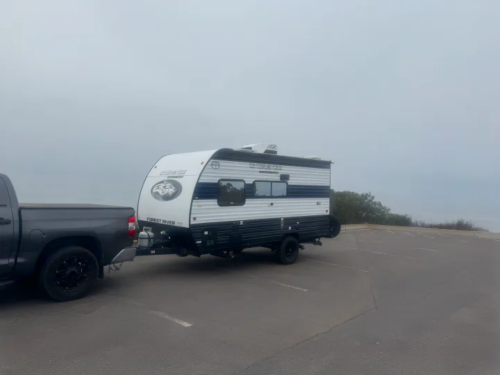 A dark gray pickup truck is hitched to a white and black Cherokee Wolf Pup travel trailer in a foggy parking lot, ready for an rv rental trip.. Forest River Wolf Pup 2025