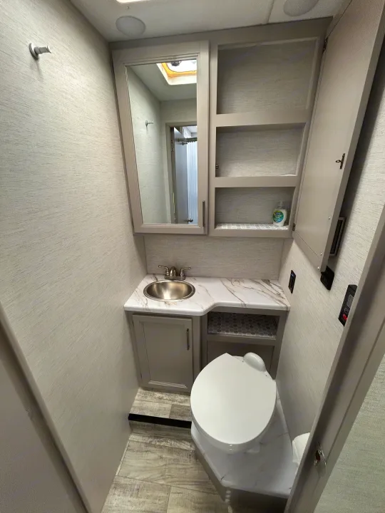 This compact RV rental bathroom showcases a sink, toilet, mirror, and a glimpse of the shower.. Thor Motor Coach Chateau 2025