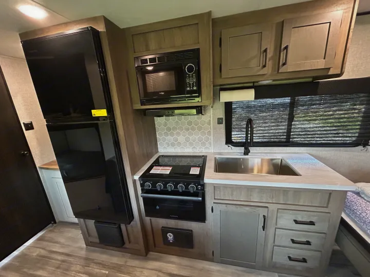 RV rental kitchen: black fridge, microwave, gas range, sink, and stylish hexagonal backsplash.. Starcraft Autumn Ridge 2025