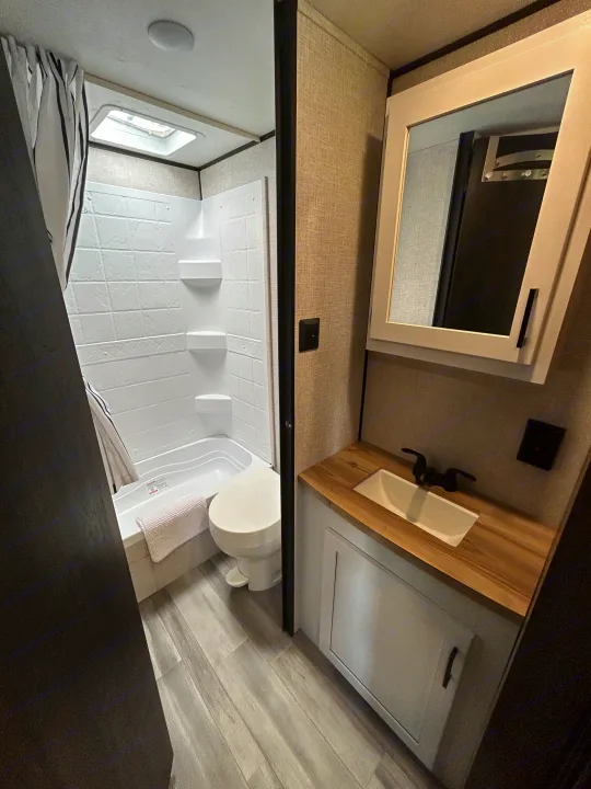 Modern RV rental bathroom with shower/tub, toilet, and vanity. Features wood-look floor, mirrored cabinet, and skylight.. Starcraft Autumn Ridge 2025