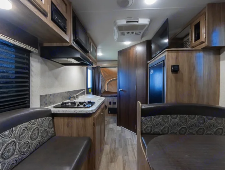 Explore this RV rental interior, featuring a well-equipped kitchen and an upholstered dinette, ready for adventure.. Jayco Jay Feather 2018