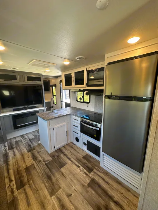 Clean RV rental interior showcasing a modern kitchen with stainless appliances, and a living area with TV & fireplace.. Crossroads RV Volante 2023