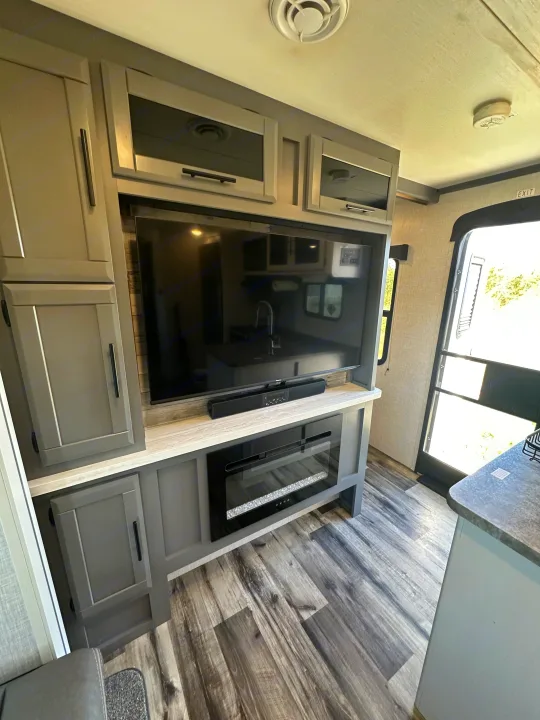 This modern rv rental interior features a grey entertainment unit with TV, soundbar, and electric fireplace, offering a cozy living space.. Crossroads RV Volante 2023