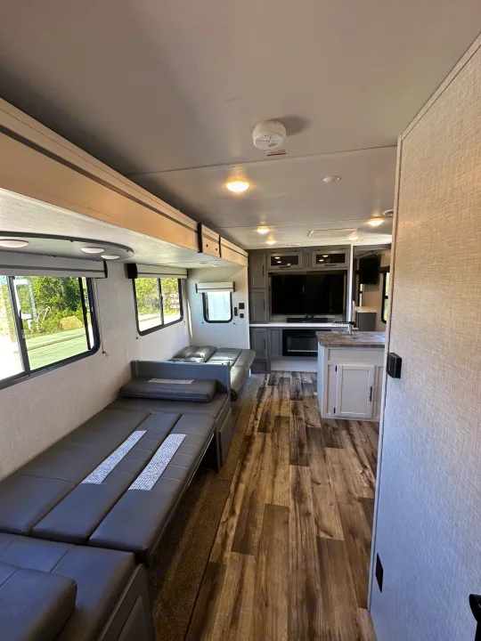 Spacious RV rental interior with grey convertible seating, wood-look floor, kitchen island, and entertainment setup.. Crossroads RV Volante 2023