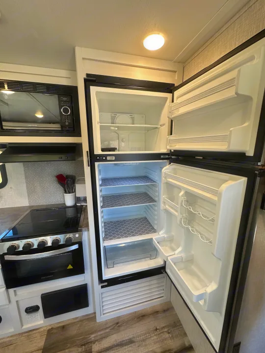 Explore this RV rental's pristine kitchen: open fridge with patterned liners, microwave, and stove. All set for your trip!. Crossroads RV Volante 2023
