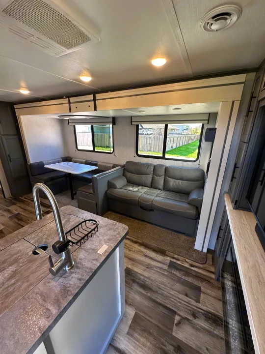 Spacious RV rental interior with a modern kitchen area, dining booth, and comfortable sofa, featuring wood-look flooring.. Crossroads RV Volante 2023