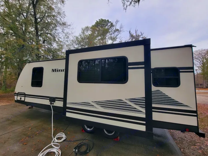 RV rental travel trailer parked at a campsite, slide-out extended, with water and power hookups connected. Ready for adventure.. Winnebego Minnie Winnie 2020