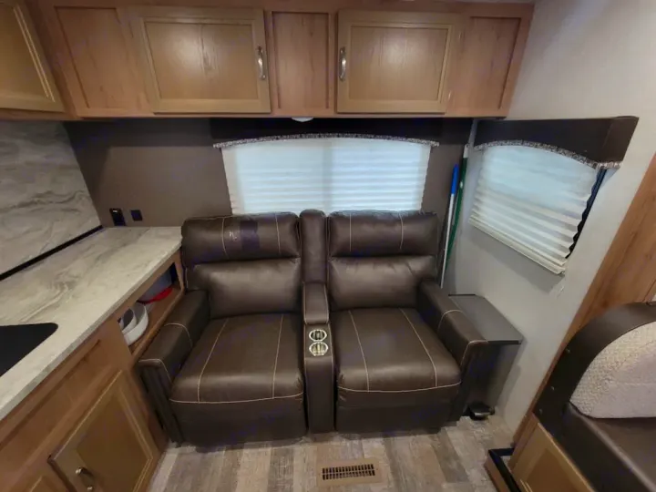 Cozy RV rental interior featuring comfy brown recliners with cup holders, a kitchen counter, and ample overhead storage.. Winnebego Minnie Winnie 2020