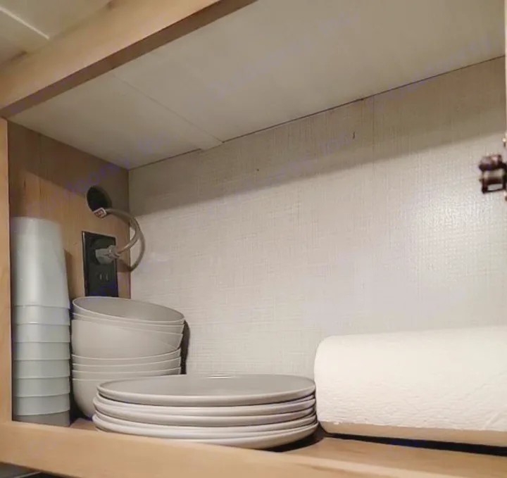 RV rental kitchen cabinet: Organized gray dishes, cups, bowls, & paper towels inside. Power outlet visible.. Winnebego Minnie Winnie 2020