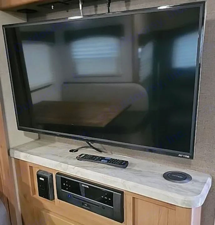 Inside an RV rental: A flat-screen TV, CONEX entertainment system, remote, and wireless charger on a marble-look counter.. Winnebego Minnie Winnie 2020