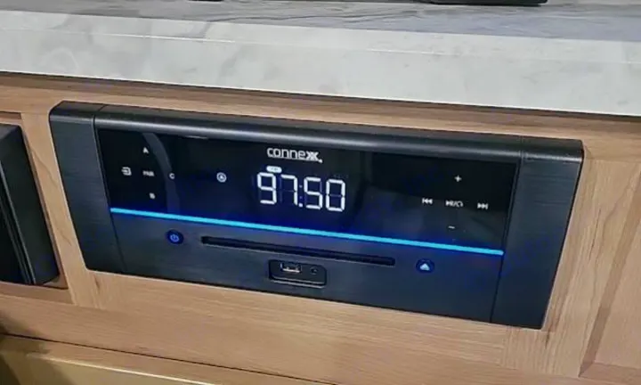 This built-in Connex RV rental stereo/radio shows "97.50" on its digital display, with blue accents, in a wooden cabinet.. Winnebego Minnie Winnie 2020
