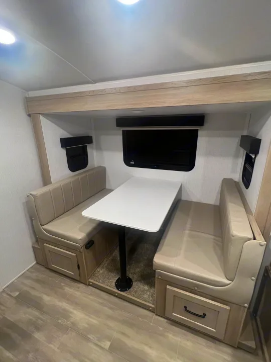 Inside an RV rental: a modern dinette with comfy bench seating, storage, table, and overhead TV for your journey.. Forest River Rockwood Geo Pro 2024
