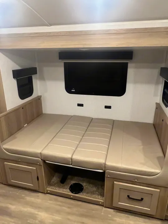 RV rental: Beige convertible dinette/bed in a compact RV interior with a wall-mounted TV and under-seat storage.. Forest River Rockwood Geo Pro 2024