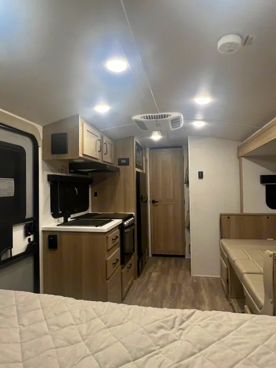 Clean RV rental interior with light wood cabinetry, a compact kitchen, versatile dining/seating area, and a bed.. Forest River Rockwood Geo Pro 2024