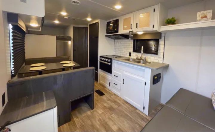This rv rental interior features a modern kitchen with a stove, sink, and microwave, alongside a cozy dining booth.. Keystone RV Hideout 2023